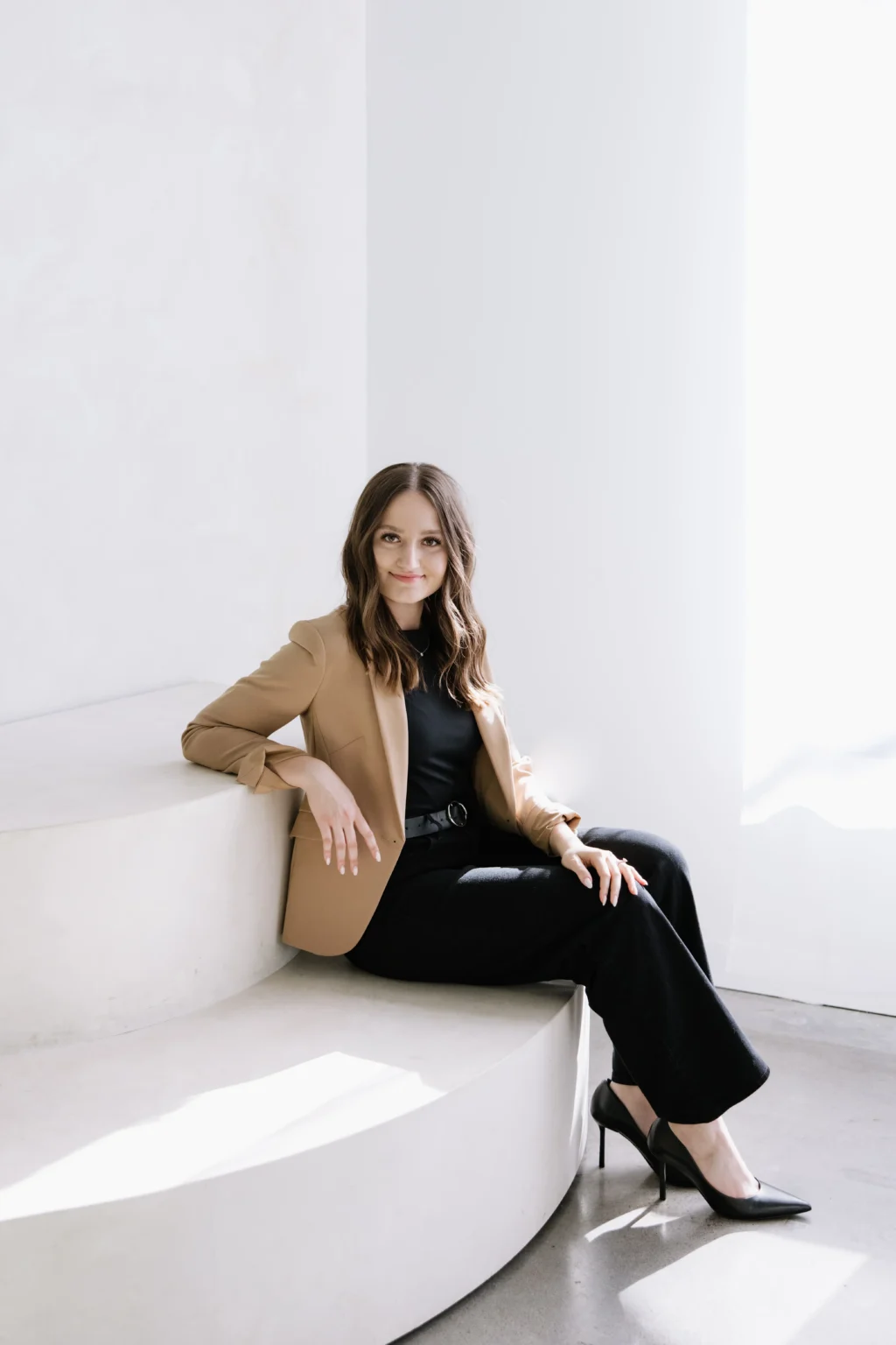 Anna hairstylist sitting on a curved white bench inside a bright modern salon studio in Lake Oswego