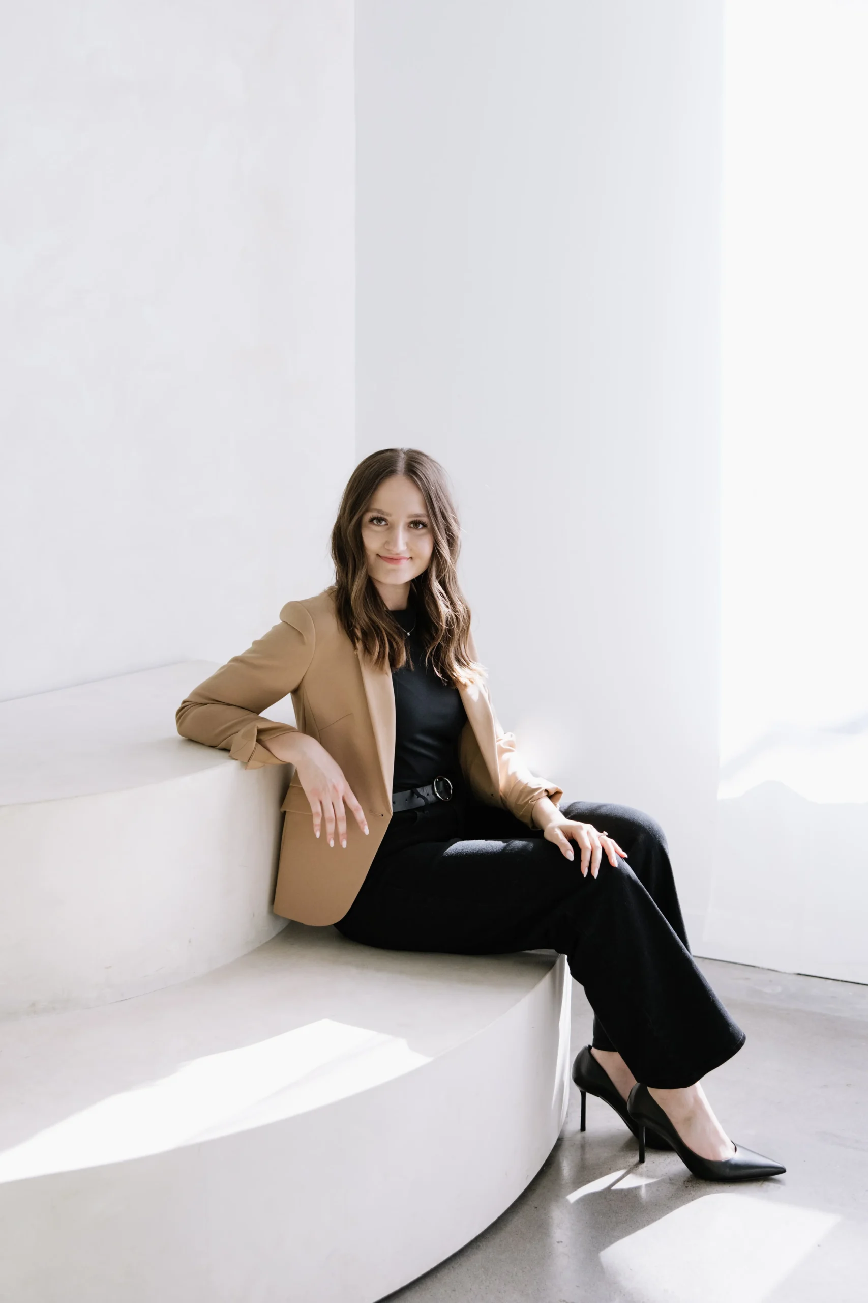 Anna hairstylist sitting on a curved white bench inside a bright modern salon studio in Lake Oswego